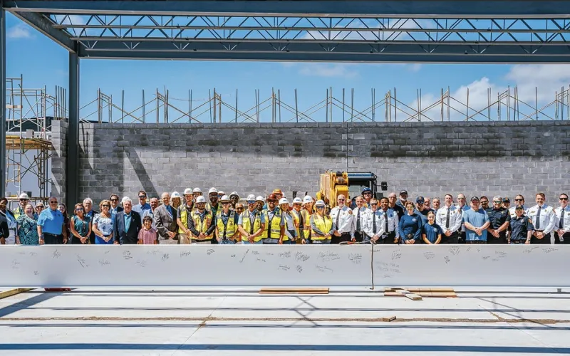 A large group of people in construction attire and formal wear stands at a building site.