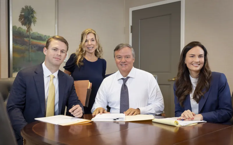 Four people in business attire smiling around a conference table.