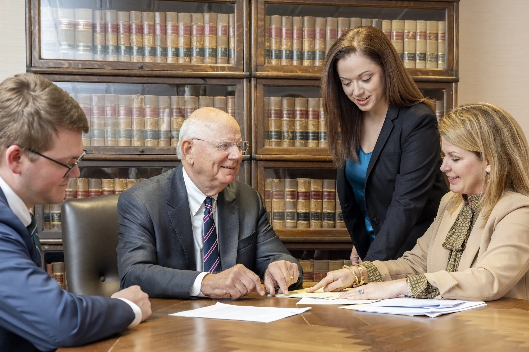 Four people in a meeting, discussing documents at a table in an office.