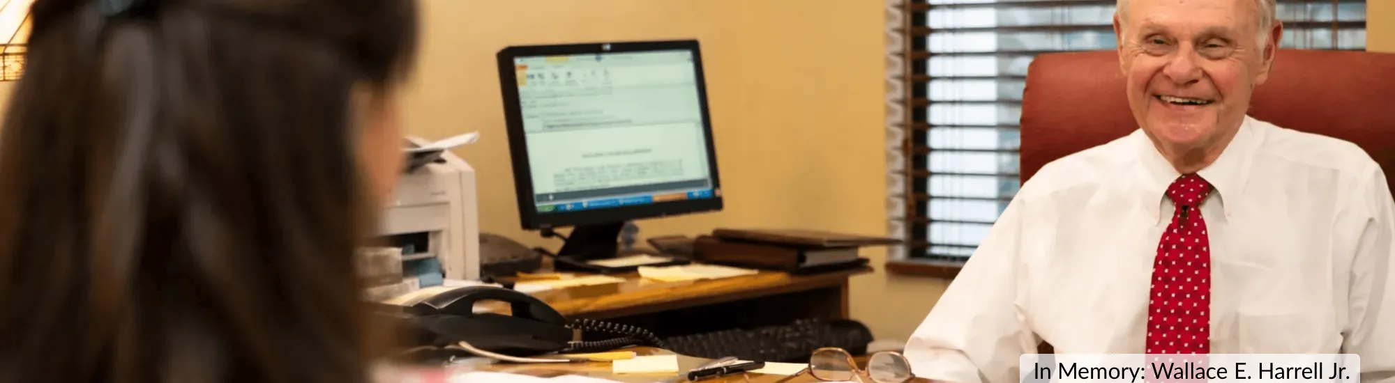 Man in white shirt and red tie smiling at a desk with a computer.